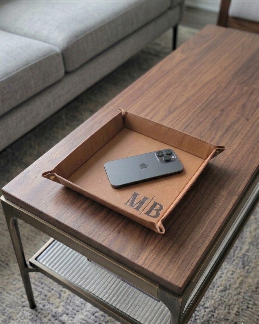 Brown leather tray with initials on a wooden coffee table, featuring an iPhone.