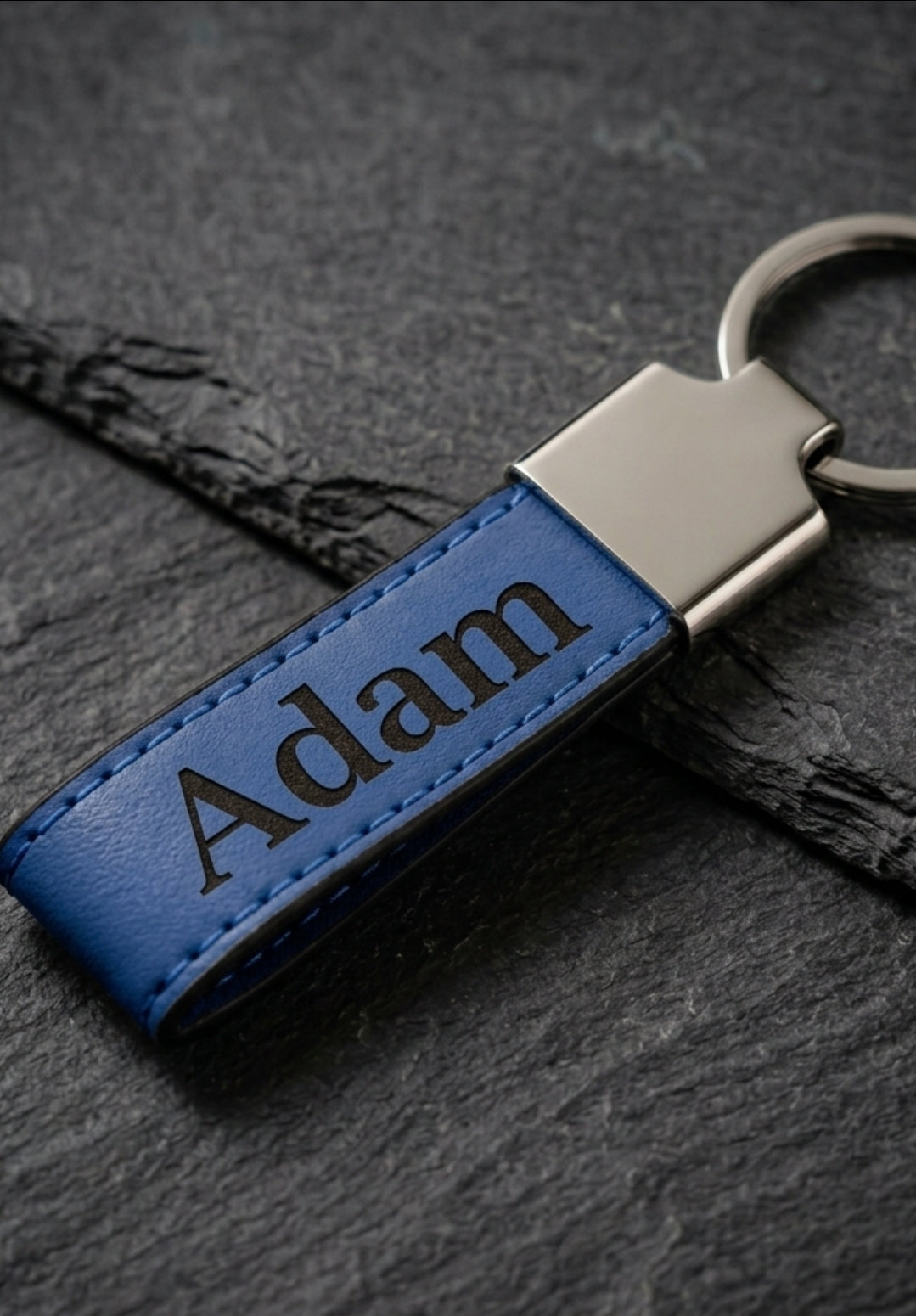 Blue leatherette keychain with the name adam engraved in black 