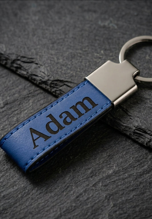 Blue leatherette keychain with the name adam engraved in black 