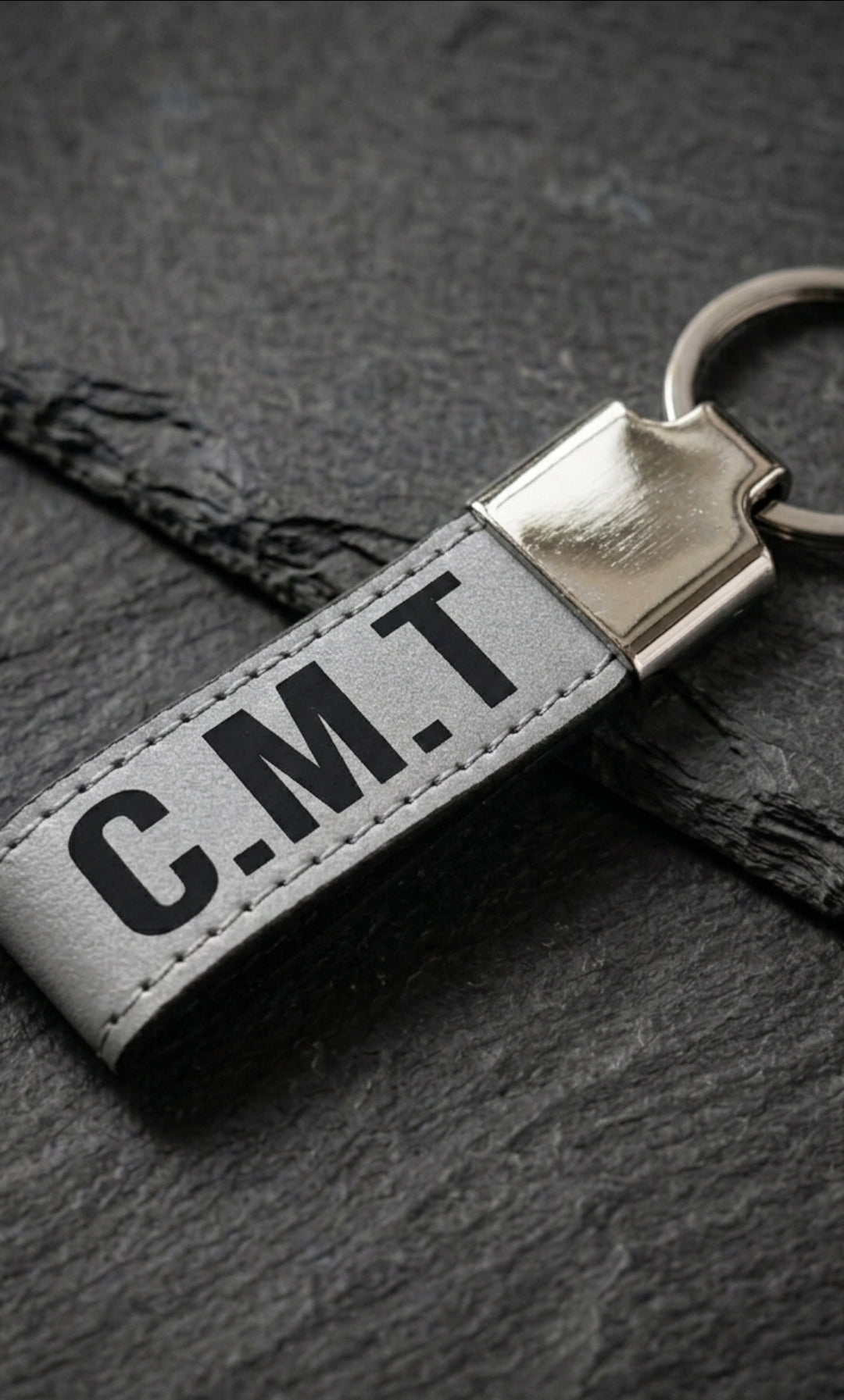 A close-up of a gray leather keychain with initials CMT engraved