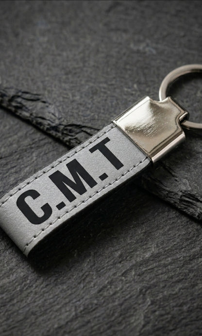 A close-up of a gray leather keychain with initials CMT engraved