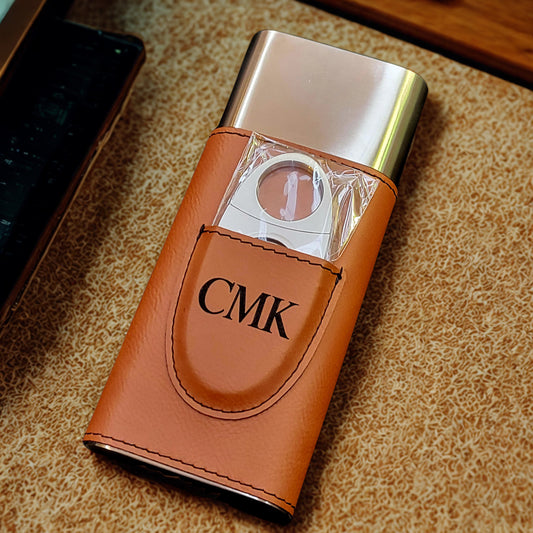 Cigarette cutter with brown leather case and gold accents on a textured surface